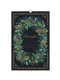 A hanging calendar page for December, featuring a dark navy background decorated with a botanical wreath in green, gold, and red tones. The word 'December' is written in elegant gold script at the center, with a small grid of dates below it.