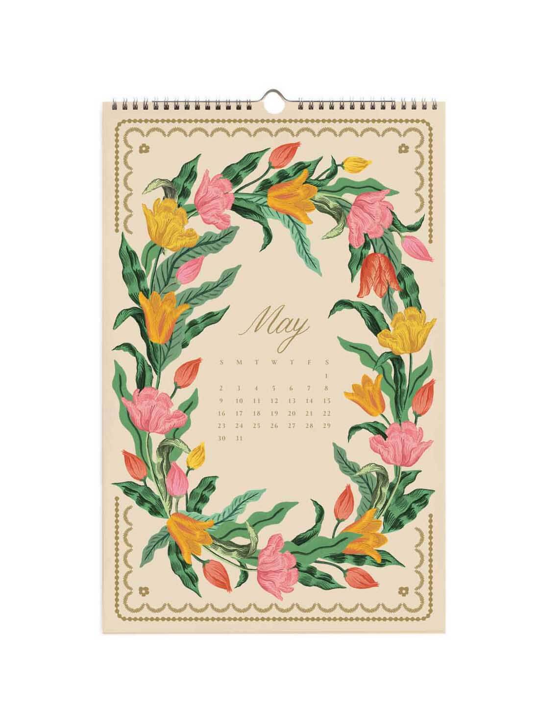 A spiral-bound May wall calendar page with a vintage floral wreath design in pink, yellow, orange, and green on a cream background, with a small calendar grid in the center.