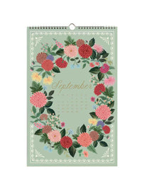 A hanging September wall calendar featuring a pastel green cover decorated with a colorful floral wreath and the word 'September' in gold script.