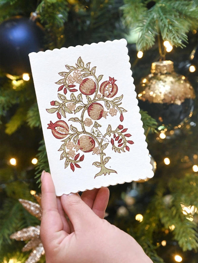 A decorative card with pomegranate design against a Christmas tree background